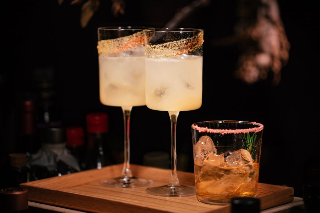 Three cocktails served in two long stemmed glasses trimmed in gold leaf and one salt rimmed rocks glass. 