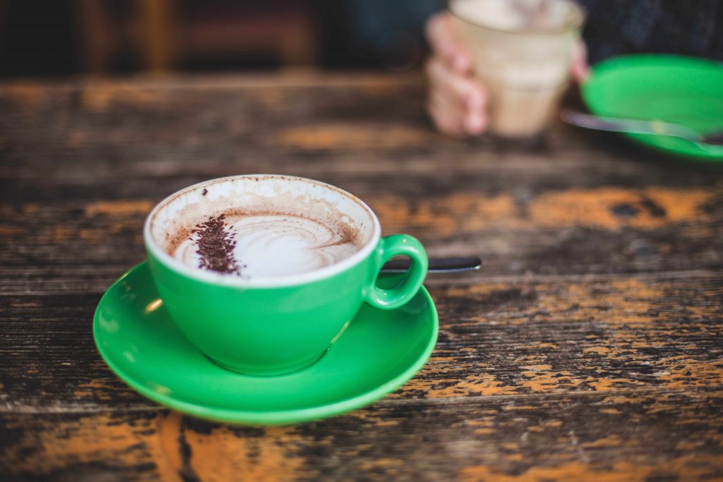 A cappuccino served in a green mug set upon a wooden table.