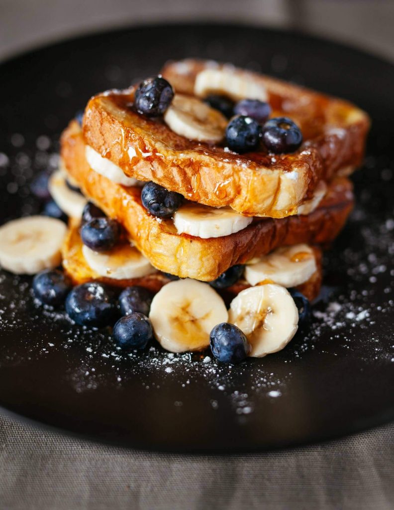 Stack of french toast layered with fresh bananas and blueberries dusted with confectioners sugar.