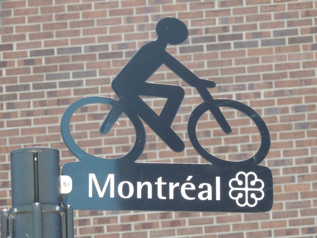 Street sign at intersection in Montréal Canada with a decorative cyclist on top.